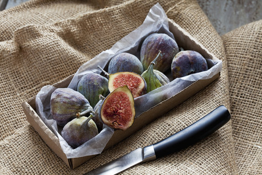 Cardboard box of figs and knife on jute