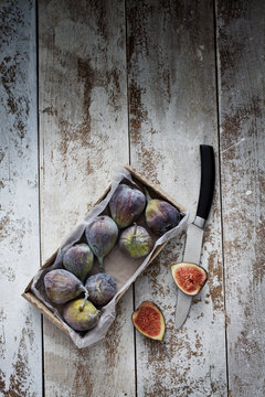 Cardboard box of figs and knife on wood