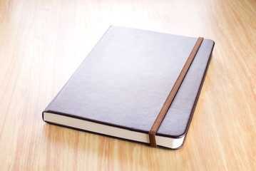 Fototapeta premium Brown Hard cover notebook with elastic strap on wooden table in