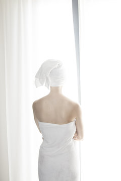 Woman wrapped in white towel standing in front of white curtain
