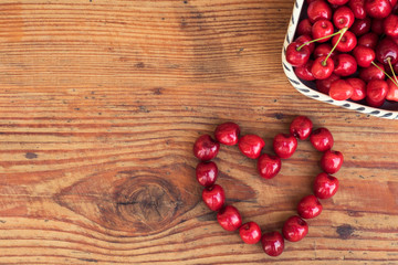 Fototapeta na wymiar Ripe organic homegrown cherries on wooden background in heart shape