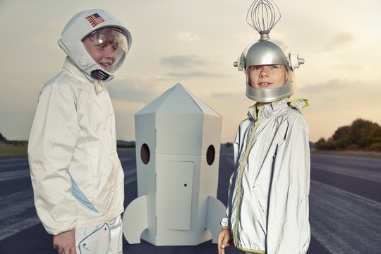 Two boys dressed up as spacemen standing at cardboard rocket