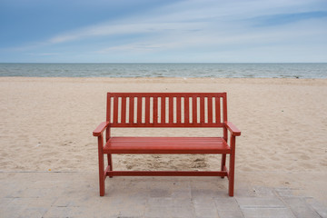 Fototapeta na wymiar Alone wooden red beach chair sitting on the sand with sea