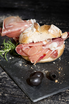 Parma ham, rolls and black olives on dark wood