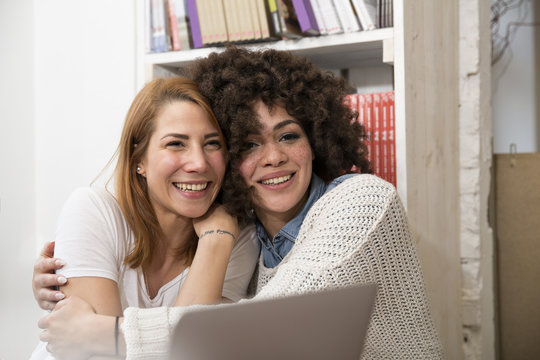 Two happy female with laptop embracing