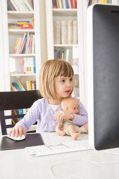 Portrait of little girl with doll spending time at computer