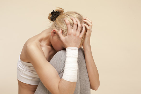 Despaired young woman sitting with head in hands and bandage around arm
