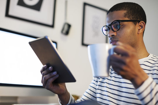 Young creative man with mini tablet having coffee break in his home office