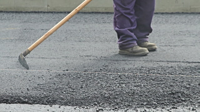 Road construction worker leveling asphalt using rake on the new road 