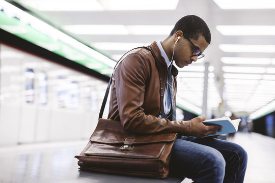 Spain, Barcelona, businessman sitting at underground station platform with book