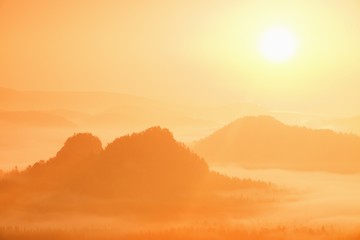 Misty landscape with fog between hills and orange sky within sunrise