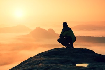 Rear view of male hiker sitting on the rocky peak  while enjoying a colorful daybreak above mounrains valley