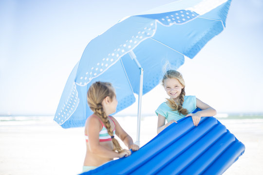 Two Girls On Beach Carrying A Lilo