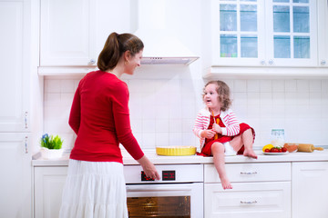 Young mother and daughter baking a pie together