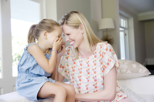 Mother and daughter sitting on sofa, giggling