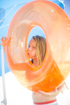 Girl on beach inflating an orange floating tire