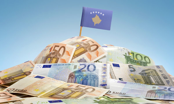 Flag of Kosovo sticking in a pile of various european banknotes.