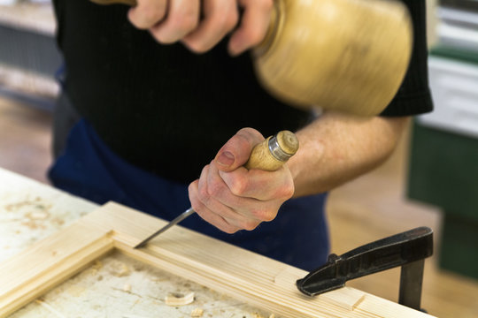 Frame-maker working on a wooden frame with mallet and chisel