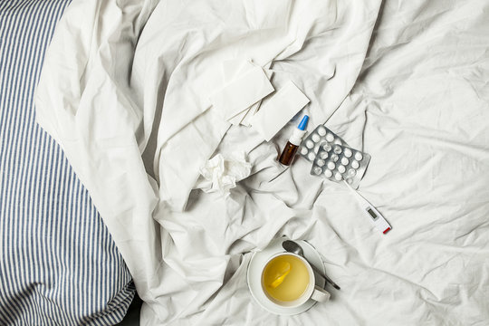 Lemon infusion, thermometer, pills, nasal spray and tissues in bed