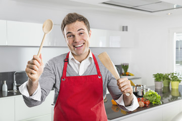 Portrait of smiling man with red apron and kitchen utensils
