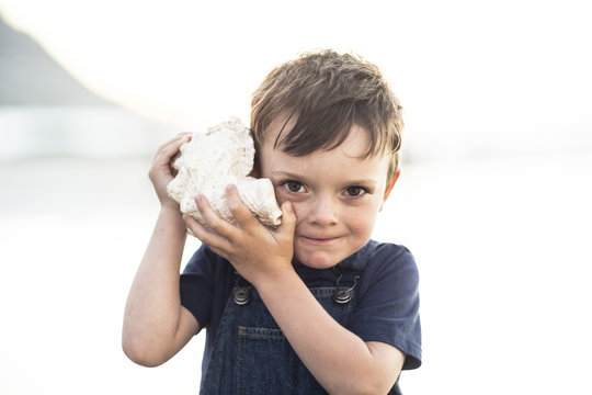 Boy on the beach listening to the sound of the ocean in a big shell