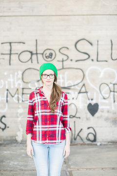 Young woman with checkered shirt and green wooly hat at graffiti wall