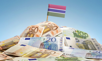 Flag of Gambia sticking in a pile of various european banknotes.