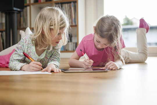 Two sisters with digital tablet and sheets of paper on floor