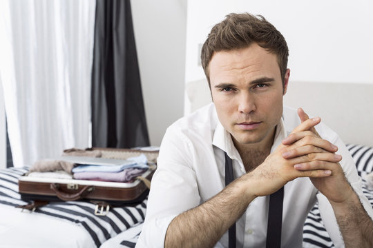 Businessman sitting on bed with clasped hands