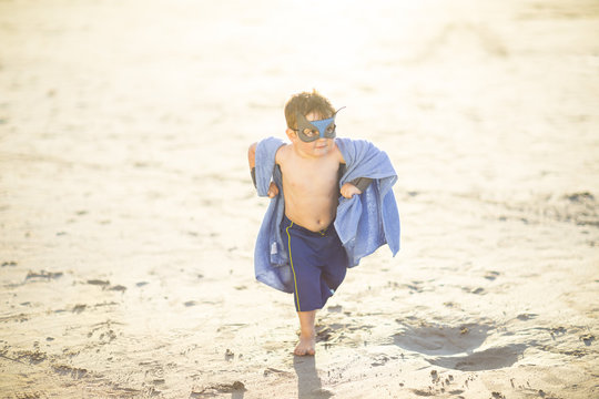 Little boy on the beach dressed up as a superhero with mask and towel