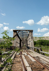 image of a very old railroad track bridge under a bright blue sky with white clouds in the summer time