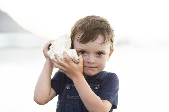 Boy on the beach listening to the sound of the ocean in a big shell