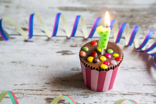 Birthday muffin with chocolate buttons and lighted candle