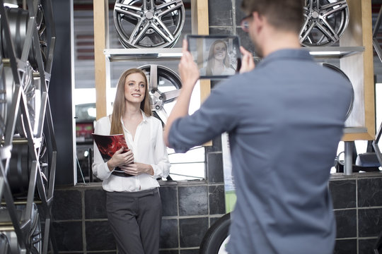 Man taking a picture of woman in a tire shop with digital tablet
