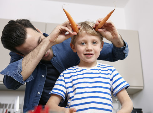 Father playing with kids in kitchen, making carrot horns