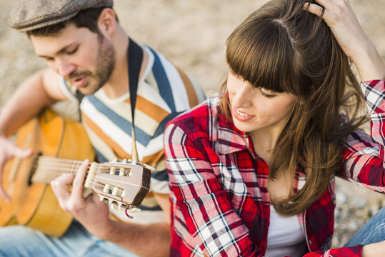 Couple sitting by the riverside, playing guitar