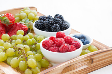 wooden tray with fresh berries and grapes on white table