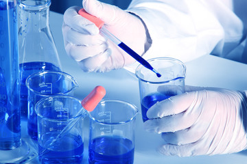 Flask in scientist hand with dropping liquid to test tube
