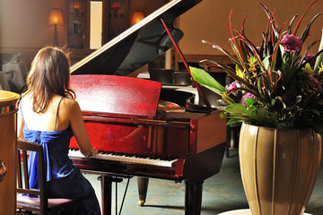 室内でグランドピアノを弾く女性の後ろ姿