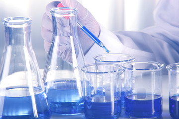 Flask in scientist hand with dropping liquid to test tube