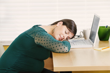 Pregnant young woman resting at her desk