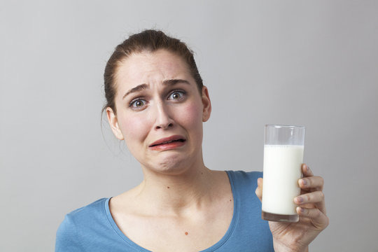scared young woman panicking at the idea of drinking a glass of smelly milk or disgusting white beverage