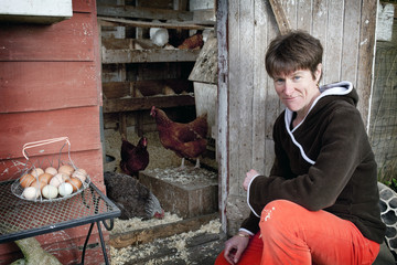 Woman kneeling at the door of her chicken coop with chickens and eggs in the background. © michaelcourtney