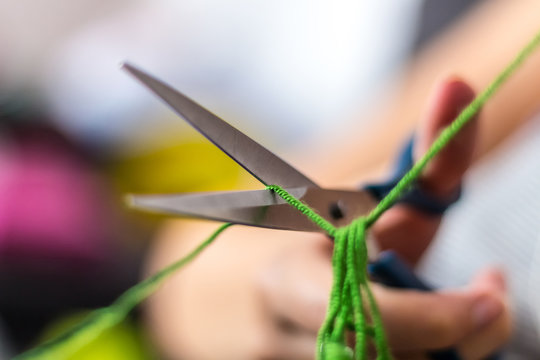 Hand Holding A Scissor And Cutting Green Thread