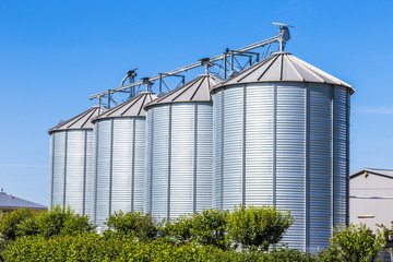four silver silos in field under bright sky