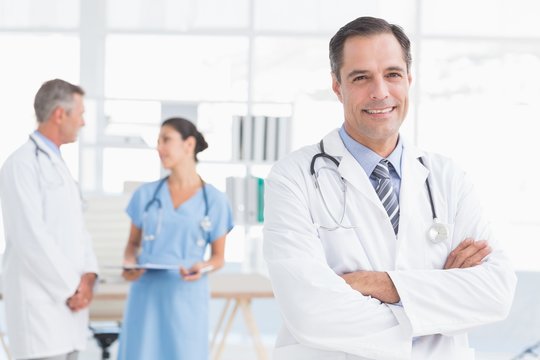 Doctor looking at camera while his colleagues works
