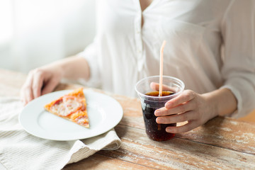 Midsection of woman with pizza slice and cola soda drink