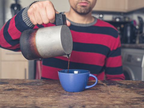 Young man pouring coffee in kitchen