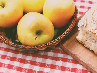 Picnic with bread on wooden cutting board and apples in a basket on red checkered table cloth