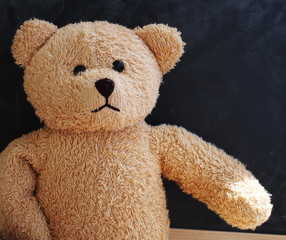 Teddy bear alone against the black board as if giving its hand to the viewer